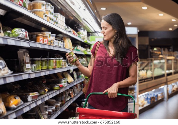 食料品店で買い物をする若い女性 スーパーで食べ物のラベルをチェックする成熟した女性 買い物かごを持つラテン女性が スーパーで商品を選ぶ の写真素材 今すぐ編集