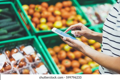 Young woman shopping healthy food in supermarket blur background. Female hands buy nature products using smart phone in store. Hipster at grocery using mobile. Person comparing price of produce - Powered by Shutterstock