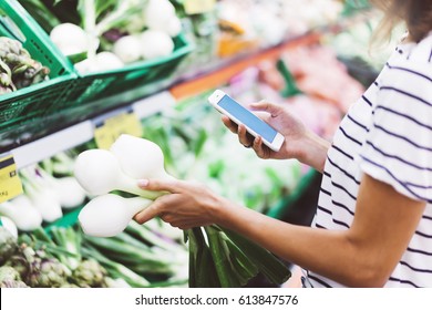 Young woman shopping healthy food in supermarket blur background. Female hands buy onion products and using smart phone in store. Hipster at grocery holding basket. Person comparing price of produce - Powered by Shutterstock