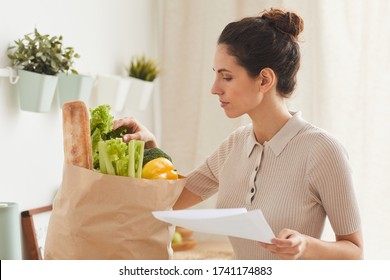 Young Woman With Shopping List Bringing Fresh Vegetables In Paper Bag To Home