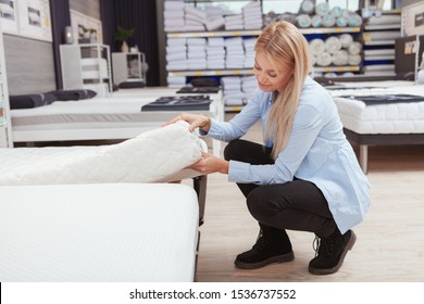 Young Woman Shopping For New Orthopedic Bed At Furniture Store, Copy Space. Female Customer Examining Mattress For Sale