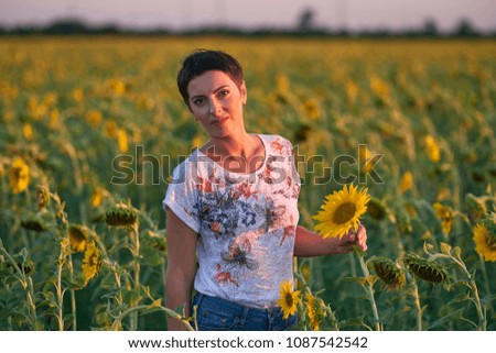 Young woman with short hair in a field of sunflowers at sunset