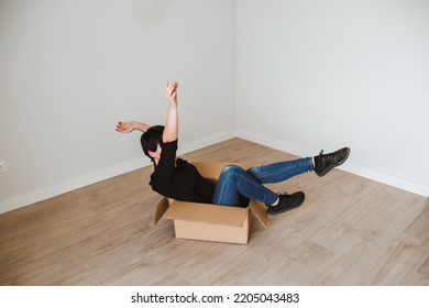 A Young Woman With Short Hair Inside A Cardboard Box In An Empty Room. Concept Of Moving And Furnishing A New Home. Solitary Life. Become Independent. Single Woman