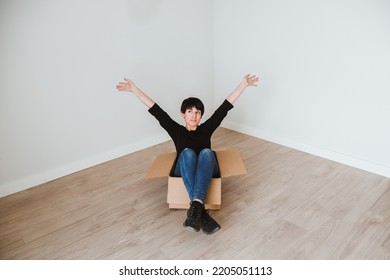 A Young Woman With Short Hair Inside A Cardboard Box In An Empty Room. Concept Of Moving And Furnishing A New Home. Solitary Life. Become Independent. Single Woman