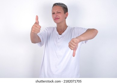 Young Woman With Short Hair Wearing White T-shirt Over White Background Feeling Unsure Making Good Bad Sign. Displeased And Unimpressed.