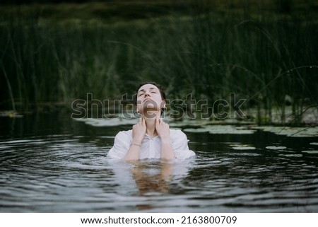 A young woman with a short haircut swims in a forest lake. Portrait