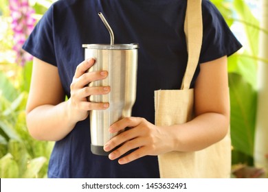 Young Woman Show Reusable Glasses Of Water In Her Hand With Green Garden Background.Use Water-glass And Steel Straw For Replacement Plastic Cup Can Save The Earth.Reduce Global Warming Concept.