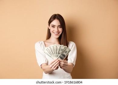 Young Woman Showing Dollar Bills And Smiling, Standing With Money On Beige Background. Concept Of Loan And Insurance