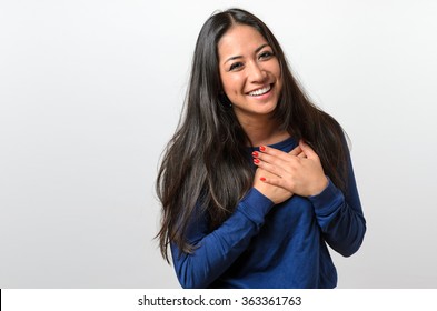 Young woman showing her heartfelt gratitude and thanks clasping her hands to her heart with a pleased smile