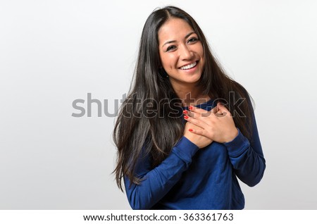 Young woman showing her heartfelt gratitude and thanks clasping her hands to her heart with a pleased smile