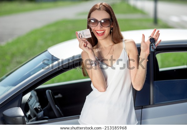 Young woman showing a key and\
license in front of the car. Girl pass successfully driving\
exam.