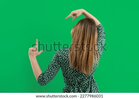 Young woman showing loser gesture on green background, back view