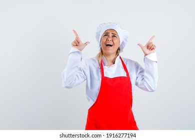  young woman showing loser signs in red apron and white hat and looking excited , front view.  - Shutterstock ID 1916277194