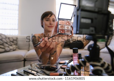Young woman showing a makeup palette on camera and recording her video. Woman making a video for her beauty blog on cosmetics.