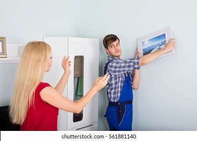 Young Woman Showing Male Carpenter For Hanging Picture Frame On Wall At Home