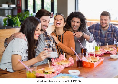 Young Woman Showing Mobile To Cheerful Friends In Restaurant