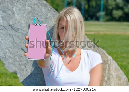 Young woman showing smartphone blank screen while sitting on grass in park on weekend
