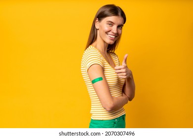 Young Woman Showing Thumb Up And Another Arm With Band Aid After Coronavirus Vaccine Injection. Covid 19 Vaccination Concept