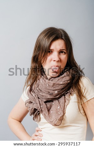 Young woman showing tongue. On a gray background.