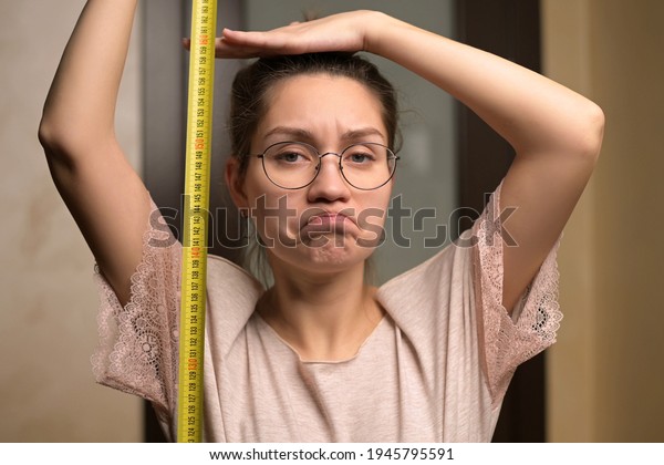 A young woman shows sadness at her height by\
holding a measuring tape next to her. The growth of a short woman\
and negative emotion