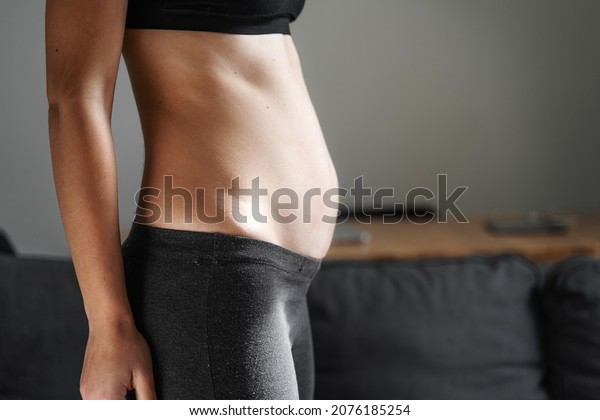 Young woman side view of body. Swollen belly. Pregnancy.\
Diastasis recti after child birth. Fitness exercises and diet for\
weight loss. 