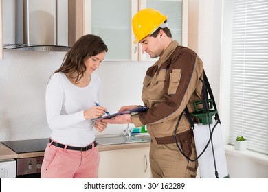 Young Woman Signing Document In Front Of Male Exterminator In Kitchen