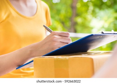 Young Woman Signing Document While Receiving Package - Courier And Delivery Service Concepts