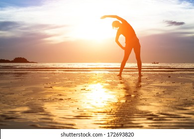 Young Woman Silhouette Exercise On The Beach At Sunset.