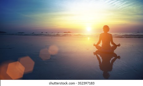 Young woman silhouette practicing yoga on the beach at amazing sunset.
