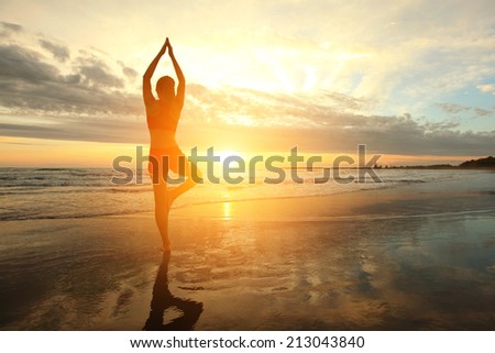 Young woman silhouette practicing yoga on the sea beach at sunset