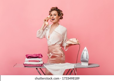 Young Woman In Silk Blouse Is Talking On Phone And Posing While Ironing Clothes