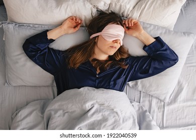 A Young Woman In A Silk Sleepwear Sleeping In A Bed With Eyes Covered With Pink Mask. Overhead View