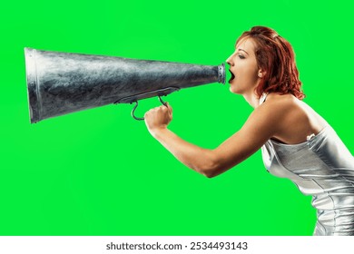 Young woman in a silver dress is using a megaphone to make an announcement on a green screen background. She is yelling into the megaphone with intensity - Powered by Shutterstock