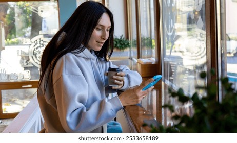 A young woman sipping coffee and browsing on her phone inside a cozy café during the morning hours - Powered by Shutterstock