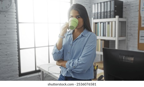 Young woman sipping coffee in a modern office setting with organized shelves, a desktop, and ample sunlight streaming through large windows. - Powered by Shutterstock