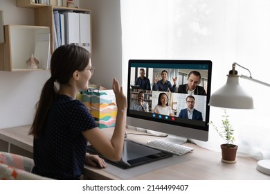 Young woman sit at desk in front of pc, looks at screen, wave hand greeting diverse friends, multinational colleagues start or finish group video call. Virtual meeting, remote communication concept - Powered by Shutterstock