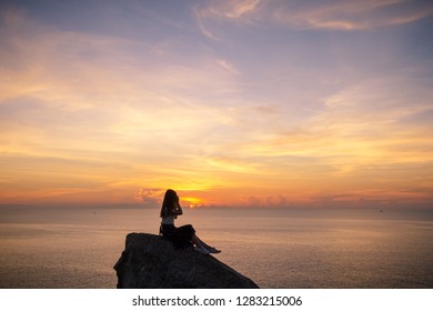 young woman sit on stone and use mobile phone takes a photo with beautiful amazing sea sunset of orange red colors - Shutterstock ID 1283215006