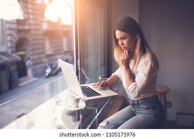 Young woman siting at cafe drinking coffee and working on laptop
