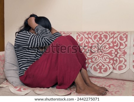 A young woman sits alone on a couch, her head downcast in a look of disappointment or sadness. Perhaps she is experiencing a setback, heartbreak, or loneliness
