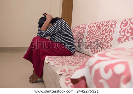 A young woman sits alone on a couch, her head downcast in a look of disappointment or sadness. Perhaps she is experiencing a setback