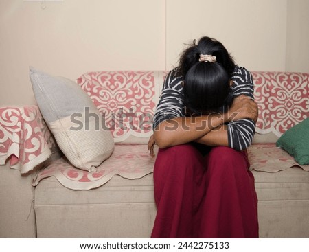 young woman sits alone on a couch, her head downcast in a look of disappointment or sadness