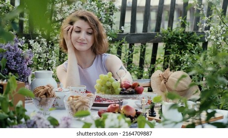 A Young Woman Sits In The Backyard At A Table With Ripe Organic Berries And Pastries. Summer Holiday Concept