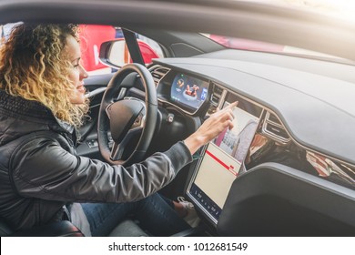 Young Woman Sits Behind Wheel In Car And Uses An Electronic Dashboard, Tablet Computer. Girl Is Traveler Looking For A Way Through Navigation System. Trip, Caravanning, Tourism, Journey.