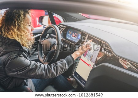 Young woman sits behind wheel in car and uses an electronic dashboard, tablet computer. Girl is traveler looking for a way through navigation system. Trip, caravanning, tourism, journey.