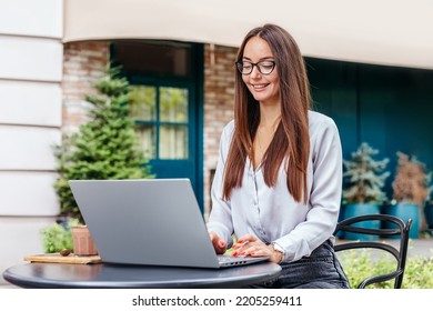A young woman sits at a cafe table, uses a laptop and looks at the screen. Search for remote work, vacancies. HR manager