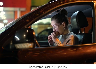 A Young Woman Sits In The Car In The Evening And Eats A Burger. Snack On The Go, Fast Food In The Car