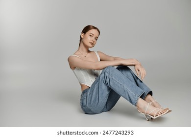 A young woman sits confidently on a white backdrop, wearing jeans and a white top. - Powered by Shutterstock