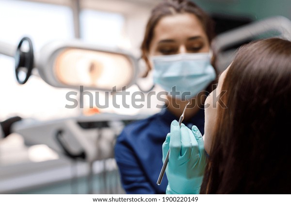 Young woman sits in the\
dentist\'s chair and the dentist carefully examines the patient\'s\
teeth. The dentist consults a patient sitting in a chair at the\
clinic