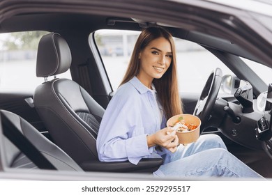 A young woman sits in her car eating a healthy salad, capturing the essence of a quick and nutritious meal during a busy day. - Powered by Shutterstock