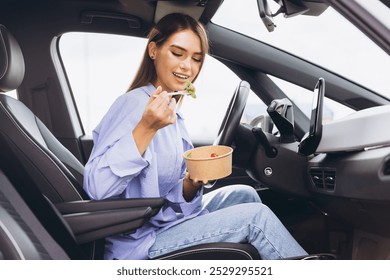 A young woman sits in her car eating a healthy salad, capturing the essence of a quick and nutritious meal during a busy day. - Powered by Shutterstock